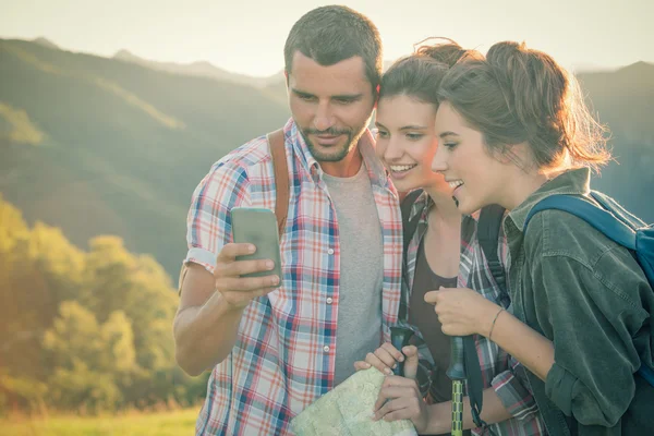 Trei prieteni se uită la smartphone pe munte la apus de soare — Fotografie, imagine de stoc