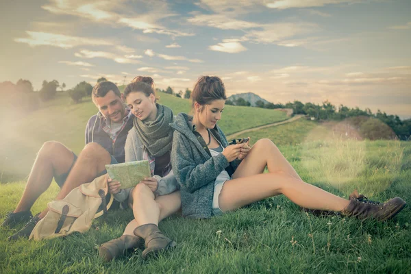 Three friends sitting on grass looking at map on mountain