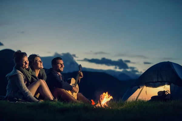 Tre amici in campeggio con fuoco sulla montagna al tramonto — Foto Stock