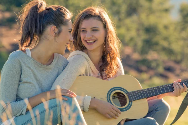 Jovem mulher cantar tocando guitarra com amigo no pôr do sol ao ar livre — Fotografia de Stock