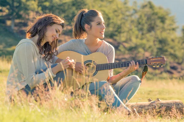 Young woman sing playing guitar with friend on sunset outdoor — Stock Photo, Image