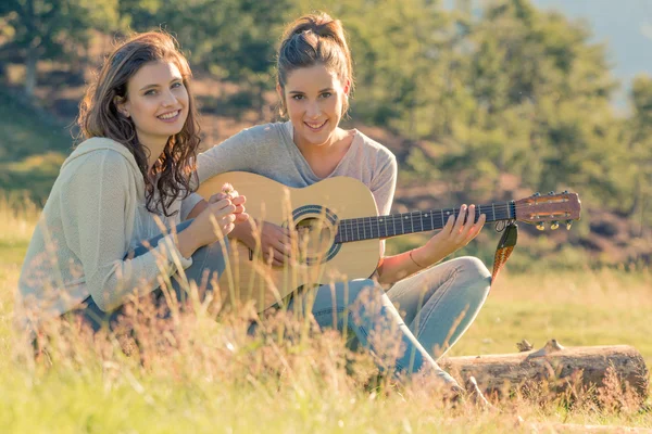 Jovem mulher cantar tocando guitarra com amigo no pôr do sol ao ar livre — Fotografia de Stock