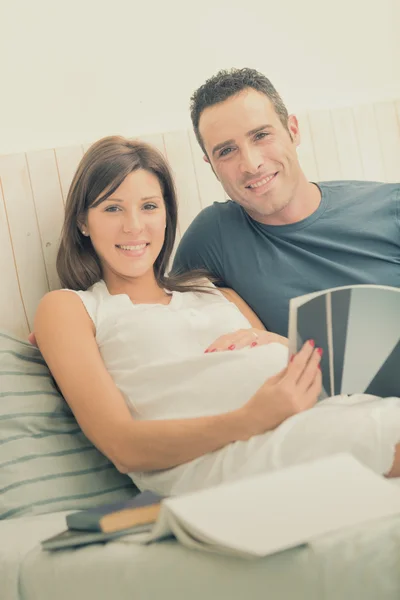 W ciąży mama brunetka z mężem czytać w łóżku — Zdjęcie stockowe