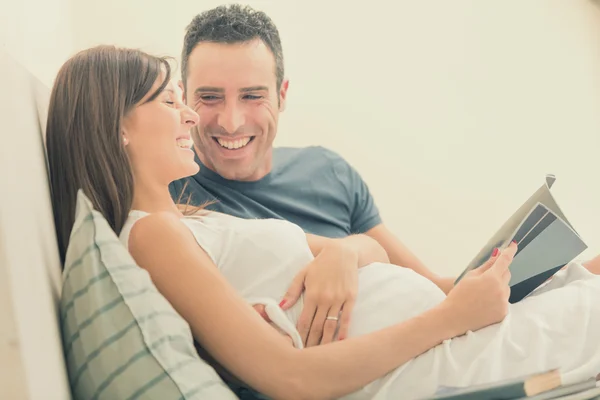 Pregnant brunette mum with husband read in bed — Stock Photo, Image