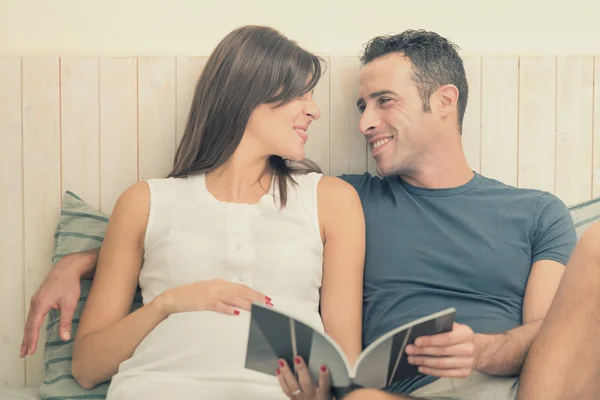 Pregnant brunette mum with husband read in bed — Stock Photo, Image