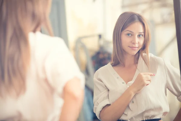 Молодая женщина смотрит в зеркальный портрет в магазине — стоковое фото