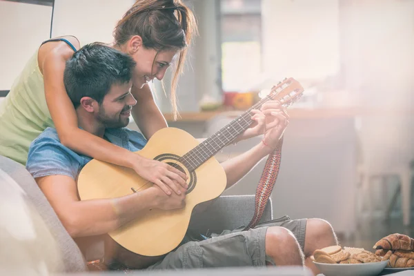 Genç çift içeride kanepede gitar çalıyor.