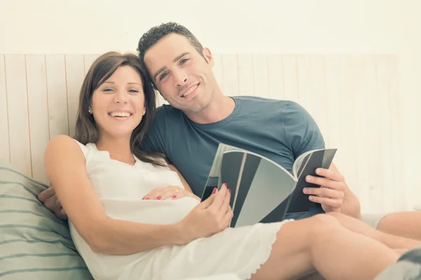 W ciąży mama brunetka z mężem czytać w łóżku — Zdjęcie stockowe