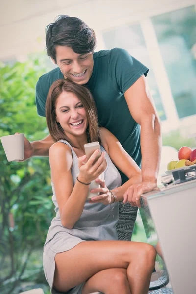 Jovem casal tomar café da manhã com smartphone na cozinha em dia ensolarado — Fotografia de Stock