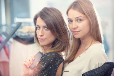 İki gülen arkadaş giyim mağazasında eğleniyor.