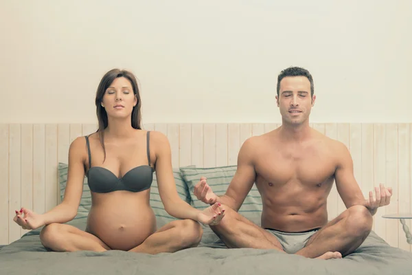 Pareja joven embarazada haciendo yoga en la cama — Foto de Stock