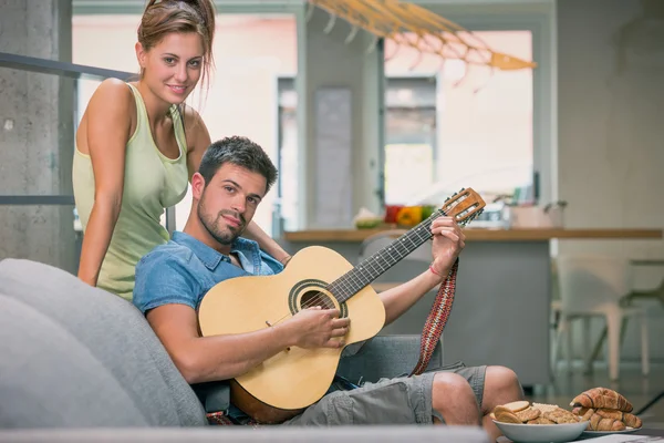 Young couple playing guitar on couch indoor — Stock Photo, Image