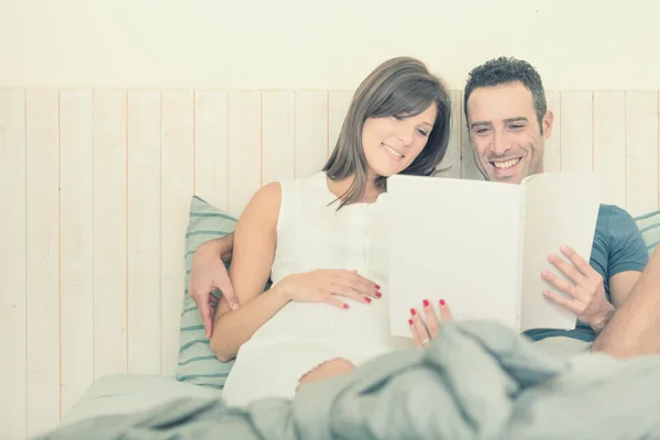 Grávida morena mãe com marido ler na cama — Fotografia de Stock