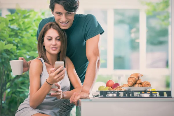 Jeune couple prendre le petit déjeuner avec smartphone dans la cuisine dans la journée ensoleillée — Photo