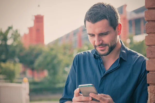 Giovane uomo barba indossa camicia blu guardando smartphone in paesaggio urbano — Foto Stock