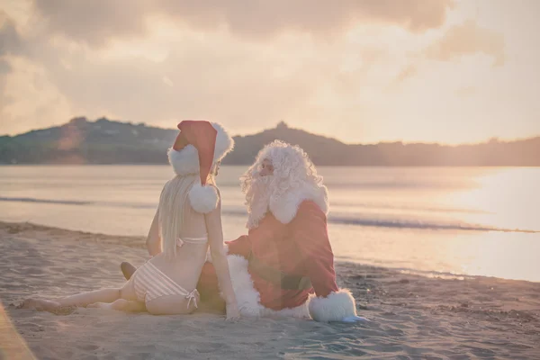 Santa Claus i dziewczyna siedzi na plaży — Zdjęcie stockowe