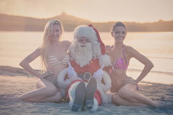 Santa Claus i dziewczyny siedzą na plaży — Zdjęcie stockowe