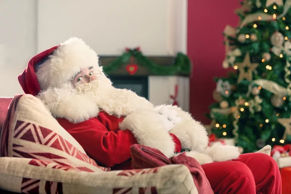 Santa Claus on couch with Christmas tree — Stock Photo, Image