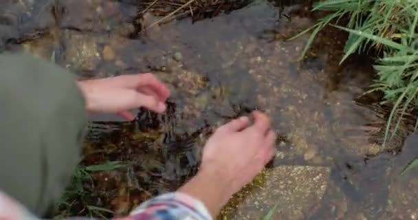 Detailní záběr mladého bělocha, jak na podzim chytá a zvedá vodu v čisté hoře. Muž si čistí ruce čistou vodou z horské řeky. — Stock video