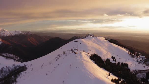 Vista aérea superior de la montaña cubierta de nieve durante el colorido atardecer al comienzo de la temporada de invierno. Valle oscuro en el fondo. cámara lenta — Vídeos de Stock