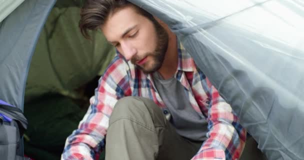 Close up of young man tying his shoes after hiking. Beautiful man relaxing in a tent with his dog. Camping and animal passion — Stock Video