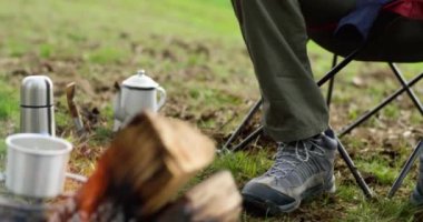 Genç adam kamp koltuğunda ateşin önünde oturup gitar çalıyor. Genç adam dinlenme kampı. Doğa, El bilgisayarı, yaşam tarzı konsepti, açık hava