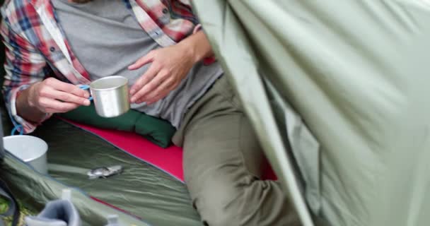 Primer plano del joven bebiendo café caliente después de hacer senderismo. Hermoso hombre relajándose en una tienda de campaña. Camping pasión — Vídeo de stock