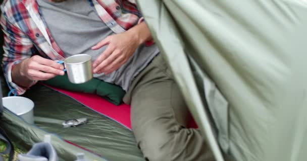 Nahaufnahme eines jungen Mannes, der nach einer Wanderung heißen Kaffee trinkt. Schöner Mann entspannt sich im Zelt. Camping-Leidenschaft — Stockvideo