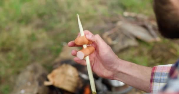Pohled zezadu na mladého muže, jak táboří a připravuje jídlo na táboráku. Káva v ohni na teplo. — Stock video
