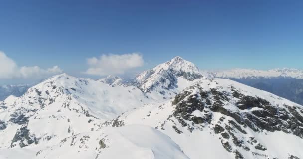 Αεροφωτογραφία της χιονισμένης οροσειράς και των κορυφών κατά τη διάρκεια μιας ηλιόλουστης ημέρας το χειμώνα. Σκοτεινό δάσος στην πλαγιά του βουνού. αργή κίνηση — Αρχείο Βίντεο