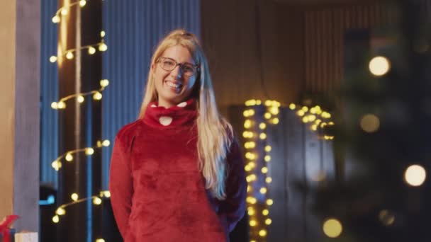 カメラを見て笑顔クリスマスの女性は、側面に髪を移動し、背景にクリスマスの装飾。クリスマスの贈り物、装飾と光 — ストック動画