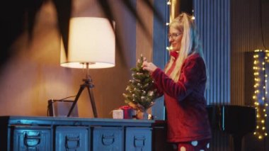 Genç bir kadın Noel kutlaması için ışık ve süslemelerle Noel ağacı hazırlıyor. Noel, evde Noel ağacı süsleyen kadın..