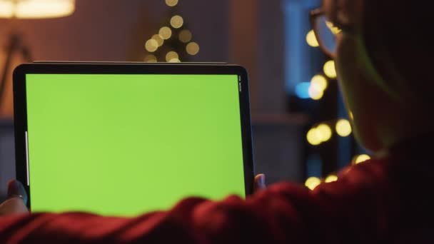 Närbild av kvinna som ligger på soffan håller och titta på sin digitala tablett under julafton.Grön skärm.Fjärrvideosamtal till jul. Slappna av hemma under julen. — Stockvideo