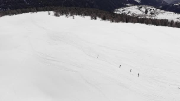 Вид зверху на повітря групи лижників, що катаються на порожньому лижному схилі в хмарах снігу. вид зверху відстеження зйомок хороших гірськолижників катання на лижах вниз по широкому лижному схилу разом. Сонячний зимовий день. повільний рух — стокове відео
