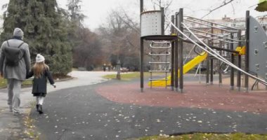 Baba ve kızının park edişinin arkası. Beyaz şapkalı ve babasıyla el ele gezen kız çocuğu bulutlu bir sonbahar yolculuğunda parklara gidiyor.