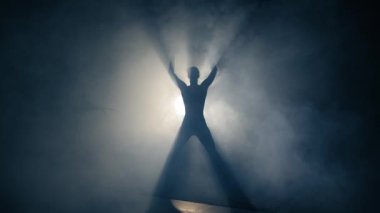 Kadın silueti spor yapıyor. Arka ışıklandırmalı kadın silueti tek başına zıplama hareketi yapıyor. Vücut geliştirme eğitimi kadın silueti. Konsantrasyon, odaklanma, enerjik kavramlar.