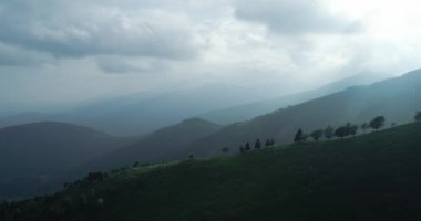 Yazın ağaçlı, el değmemiş yeşil dağın havadan görünüşü. Güneş ışığı bulutların üzerinden geçer. Arka planda sisli sıradağlar var. yavaş çekim