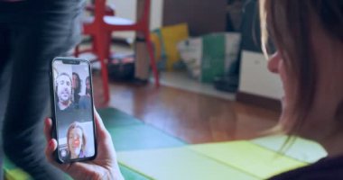 Küçük kız oturma odasında ayakta oyun oynarken, annem video için arıyor. Aile video çağrısı, uzaklık kavramları.