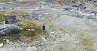 Kayalık bir dağ arazisinde tek başına koşan bir adamın havadan görünüşü. Nehir düz arazide akıyor, yerde kayalar ve çimenler.