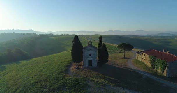 Luftaufnahme einer farbigen Landschaft in der Toskana. Die Sonne geht am Horizont.Blauer Himmel, grüner Hügel, landwirtschaftliches Feld und verlassene Kirche mit Offroad-Ausflug. — Stockvideo