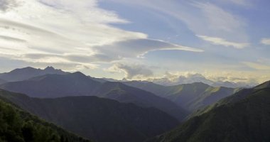 Hoş bir rüzgarla hareket eden bulutlarla birlikte dağ manzarasının hızlanması. Yazın yeşil ağaçlarla kaplı dağ zinciri. Yeşil dağ tepesinde gün batımı bulutlar hareket ediyor, güzel rüzgarlı hava..