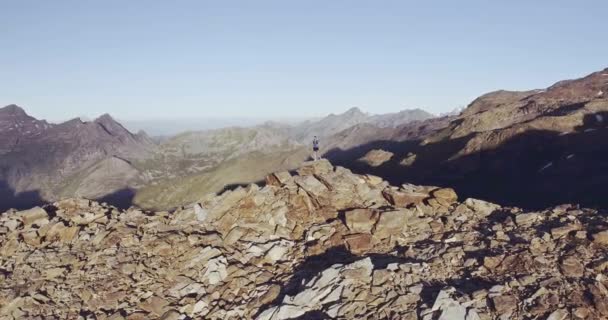 Circular aerial view of Young man hiking mountain looking at panorama on the peak at sunrise. Sense of freedom for a man standing on the top of rocky highest mountain peak.Blue t-shirt, boots,. — Stock Video