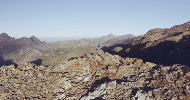 Vista aérea circular da montanha de caminhada do homem novo que olha o panorama no pico no nascer do sol. Sentido de liberdade para um homem que está no topo do pico mais alto da montanha rochoso.T-shirt azul, botas,. — Vídeo de Stock