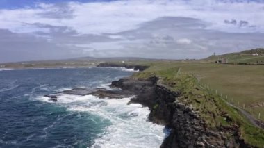 Yeşil tarlaların havadan görünüşü, çayır antenleri: yol, arka planda araba yok. Irelands tepeleri, tarlalar, ufukta bulutlar. Rüzgar ve dalgalarla hareket eden deniz..