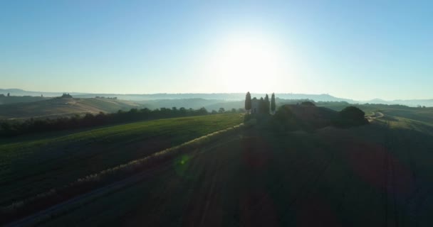Toskana 'daki renkli kırların havadan görünüşü. Güneş ufukta batıyor. Mavi gökyüzü, yeşil tepe, tarım arazisi ve terk edilmiş bir kilise.. — Stok video