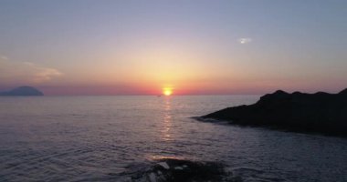 Deniz üzerindeki renkli günbatımının havadan görünüşü, Aeolian adaları. Su yüzeyine yansıyan güneş. Mor, kırmızı, mavi, turuncu alacakaranlık. Yaz günbatımında adaların silueti. Yavaş çekim