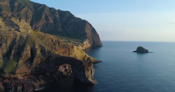 Αεροφωτογραφία της ακτής Salina, βαθύ γκρεμό, μικρό χωριό σε ένα καλοκαιρινό ηλιοβασίλεμα. Γαλάζια θάλασσα, ουρανός και άνεμος για μια γαλήνια στιγμή. Δρόμος διασχίζουν την κοιλάδα, τεράστια βουνά στο βάθος — Αρχείο Βίντεο