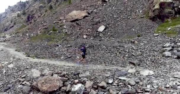 Vista aérea del joven corriendo por el camino de tierra en la costa de la montaña. Rocas alrededor del hombre practicando deporte extremo. — Vídeo de stock