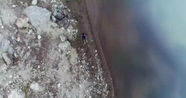 Karanlık nehrin yakınındaki çok renkli düz bir arazide koşan bir adamın yukarıdan görünüşü. Kırmızı kum, beyaz kayalar ve yerdeki çakıllar