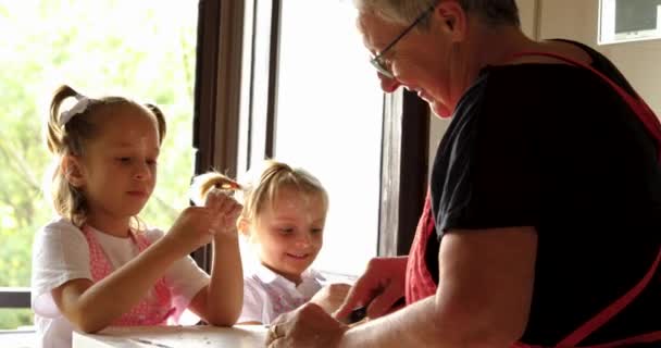 Primer plano de dos chicas cocinando pasta con la abuela. Momento divertido de dos niños aprendiendo a hacer pasta con la abuela. — Vídeos de Stock